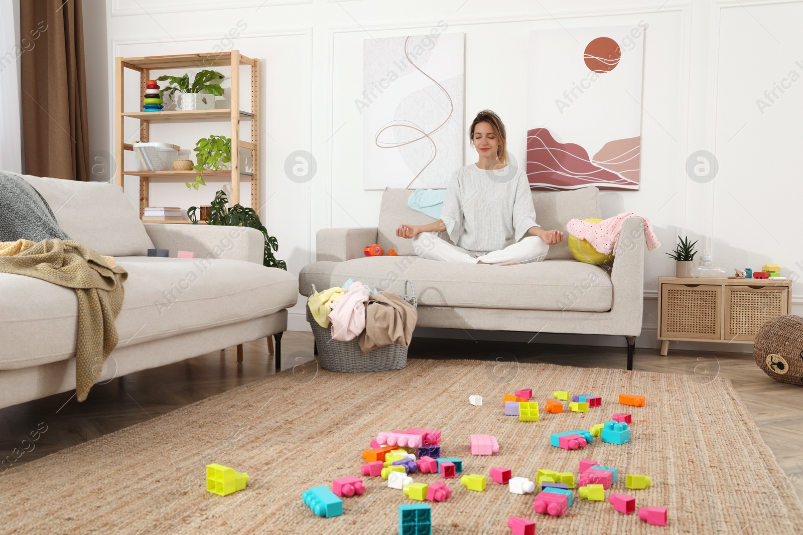 Photo of Young mother meditating on sofa in messy living room