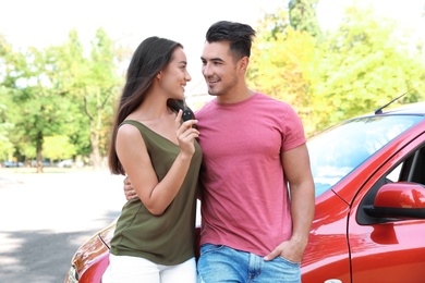 Happy young couple with key standing near new car on road