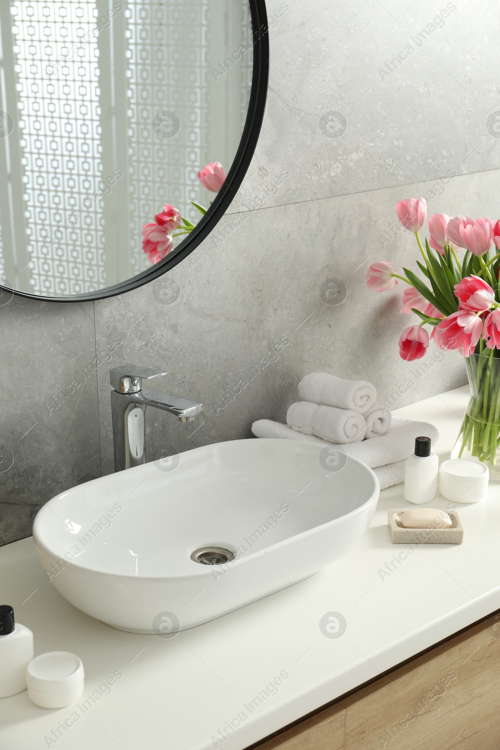 Photo of Vase with beautiful pink tulips and toiletries near sink in bathroom