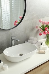 Photo of Vase with beautiful pink tulips and toiletries near sink in bathroom