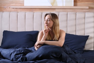 Young woman sitting on comfortable bed with silky linens