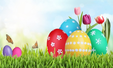 Image of Bright Easter eggs and spring flowers on green grass outdoors