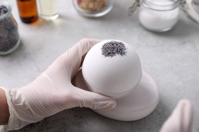 Photo of Woman in gloves with self made bath bomb at grey table, closeup