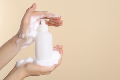 Woman with bottle of care product and cleansing foam on beige background, closeup. Space for text