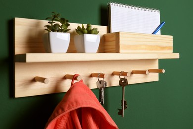 Photo of Wooden hanger for keys with clothes on green wall, closeup