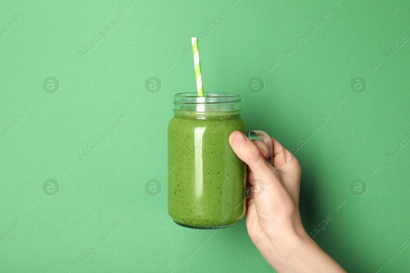 Photo of Woman holding mason jar of fresh smoothie on green background, closeup