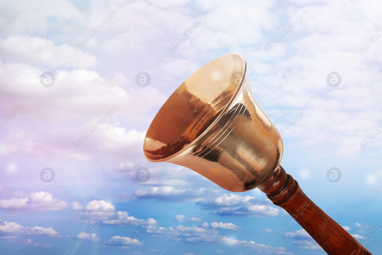 Image of Shiny school bell with wooden handle against blue sky