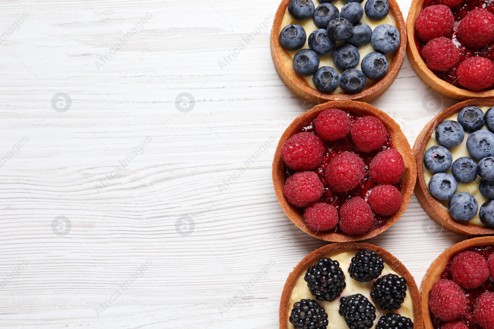 Photo of Tartlets with different fresh berries on white wooden table, flat lay and space for text. Delicious dessert