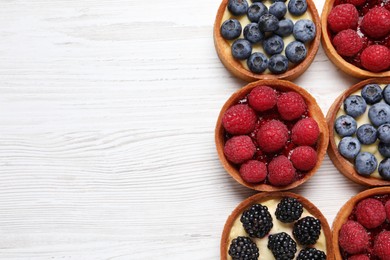 Photo of Tartlets with different fresh berries on white wooden table, flat lay and space for text. Delicious dessert