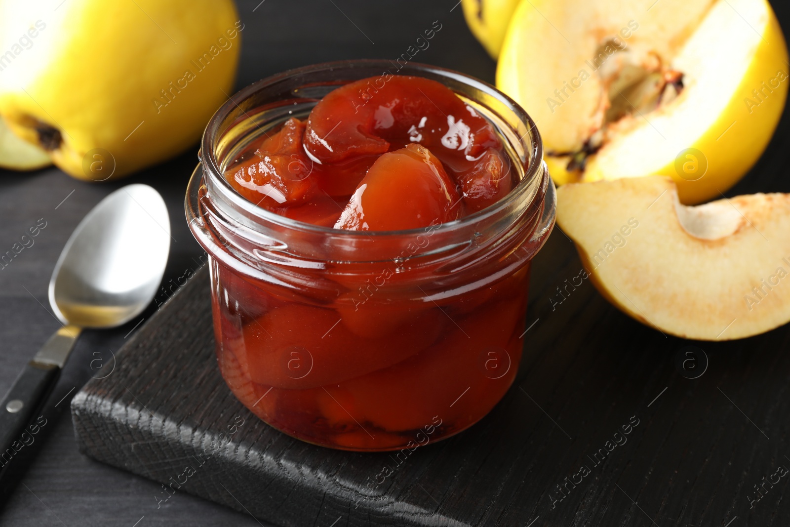 Photo of Quince jam in glass jar, spoon and fresh raw fruits on grey table, closeup