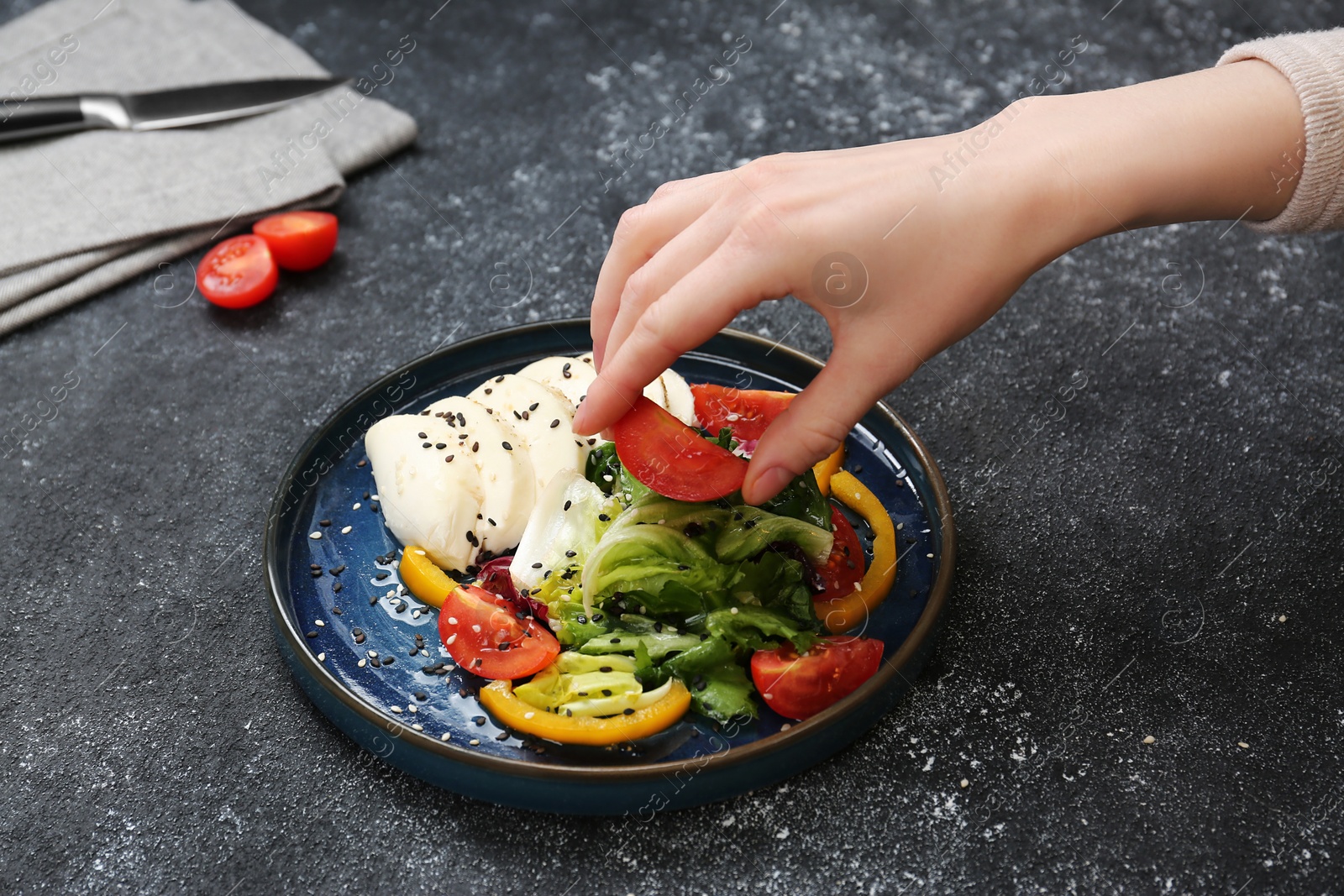 Photo of Food stylist preparing delicious salad with mozzarella and tomatoes for photoshoot at dark grey table in studio, closeup
