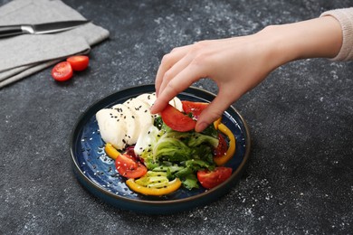 Food stylist preparing delicious salad with mozzarella and tomatoes for photoshoot at dark grey table in studio, closeup