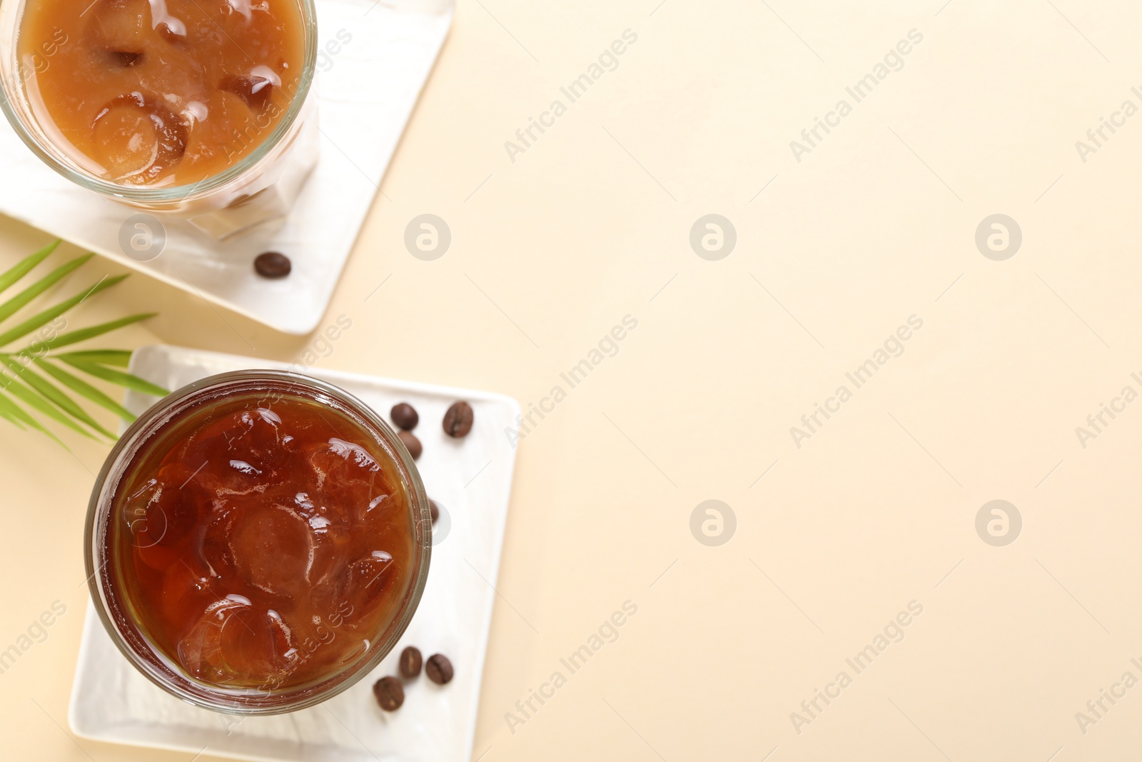 Photo of Refreshing iced coffee with milk in glasses on beige table, flat lay. Space for text