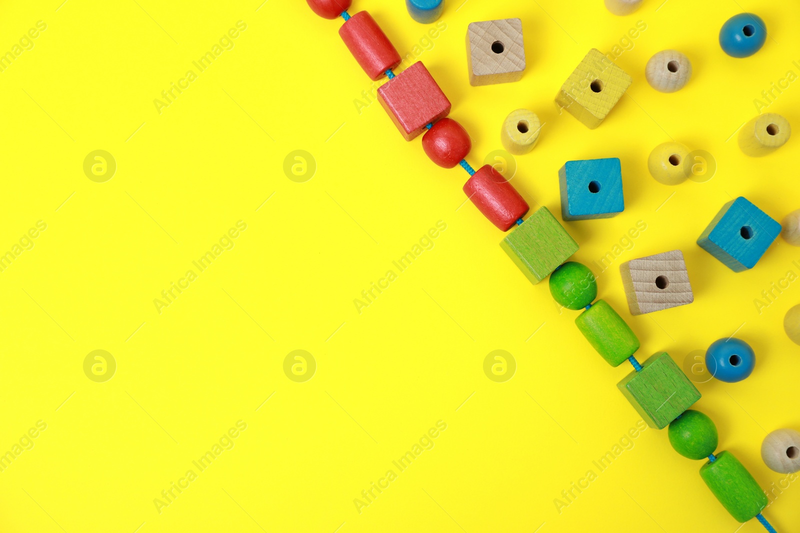 Photo of Wooden pieces and string for threading activity on yellow background, flat lay and space for text. Educational toy for motor skills development