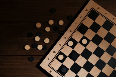 Photo of Checkerboard and game pieces on wooden table, flat lay