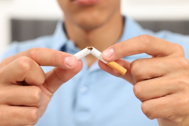 Stop smoking concept. Young man breaking cigarette on blurred background, closeup