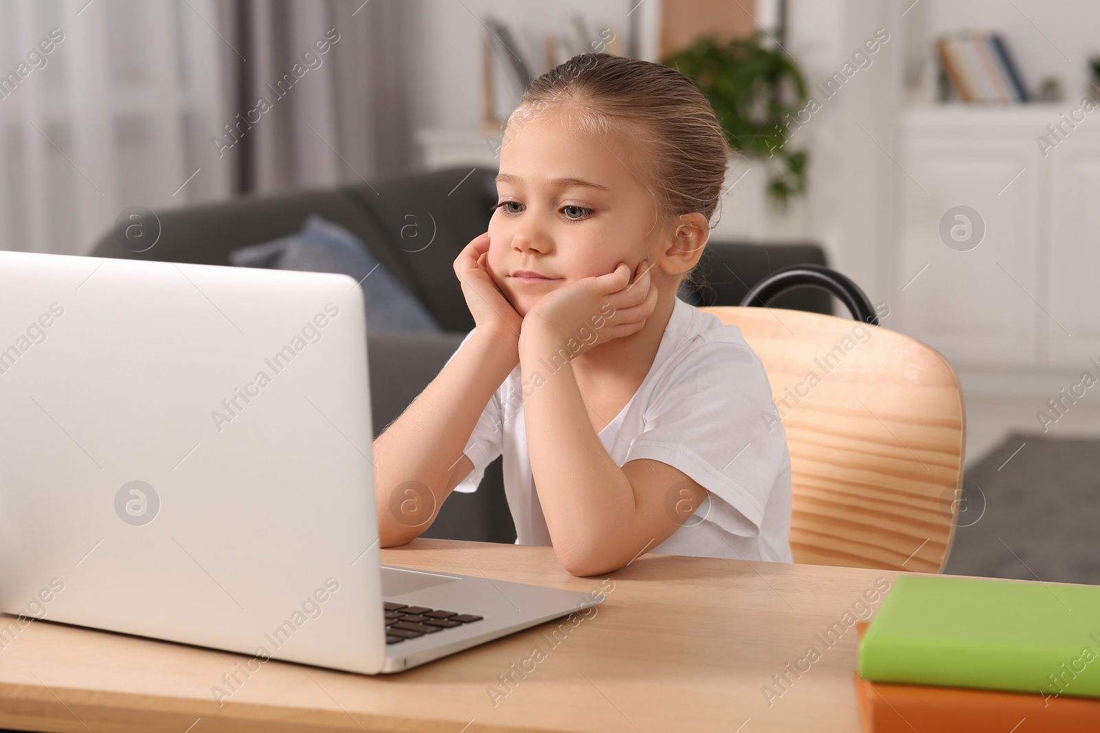 Photo of Little girl using laptop at table indoors. Internet addiction