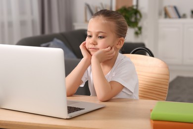 Little girl using laptop at table indoors. Internet addiction