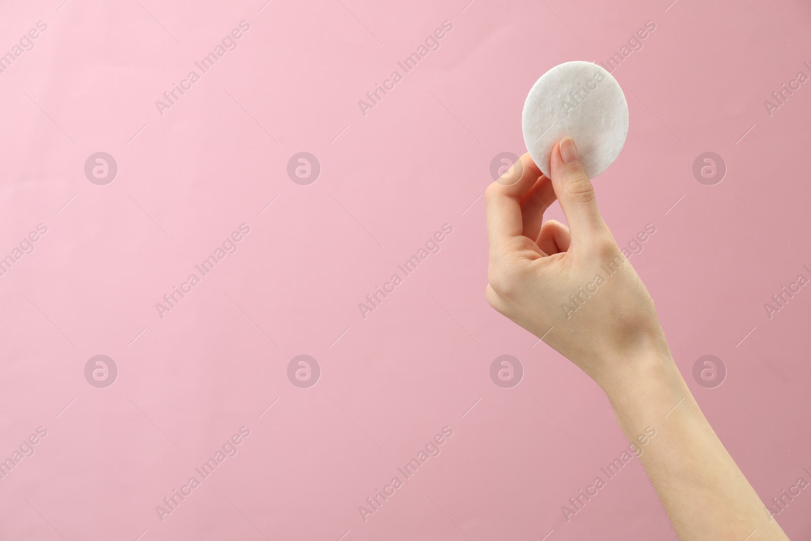 Photo of Woman holding cotton pad on pink background, closeup. Space for text