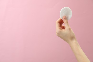 Woman holding cotton pad on pink background, closeup. Space for text