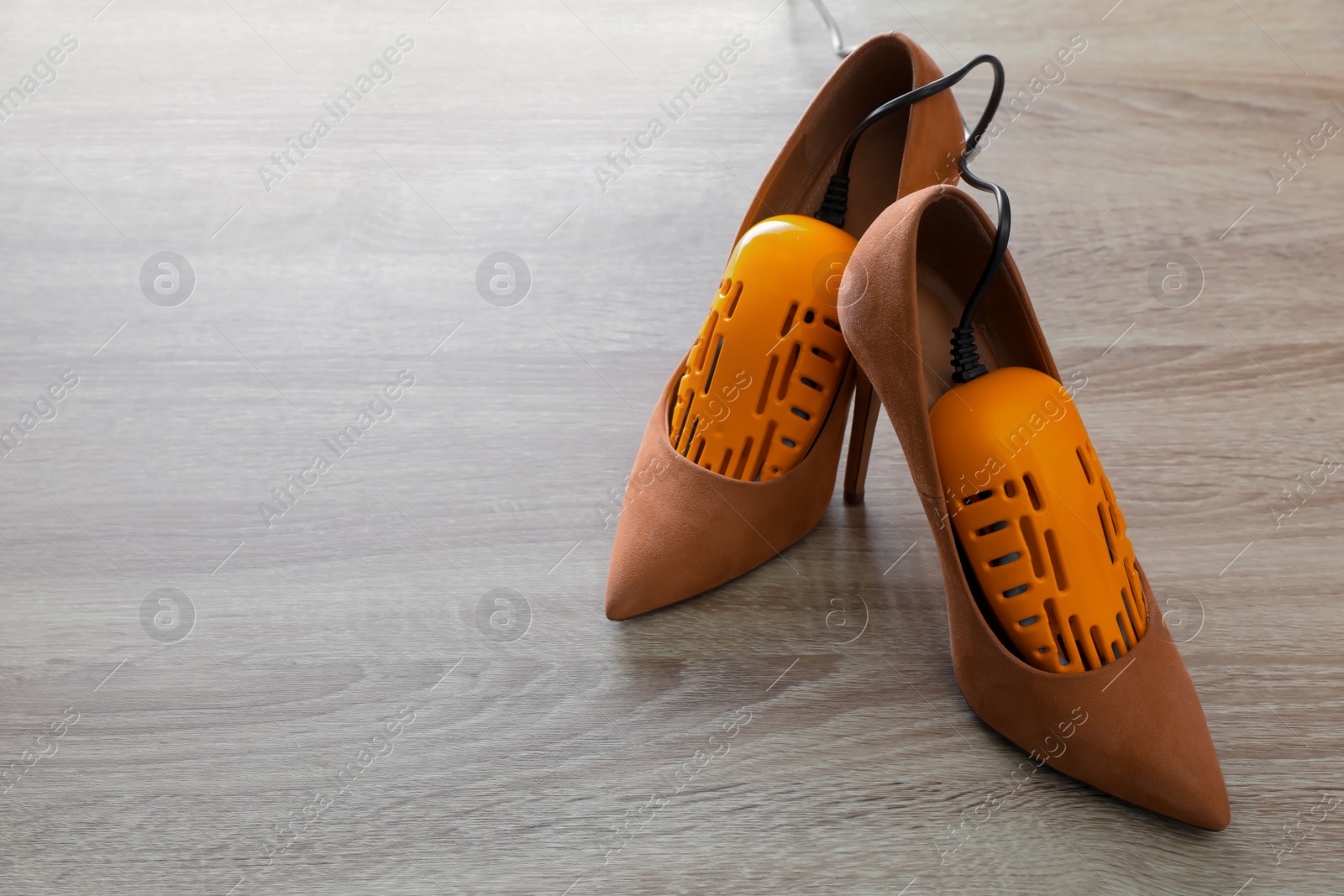 Photo of Pair of beautiful high heel shoes with modern electric footwear dryer on wooden background. Space for text