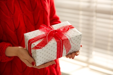 Photo of Woman holding white Christmas gift box indoors, closeup