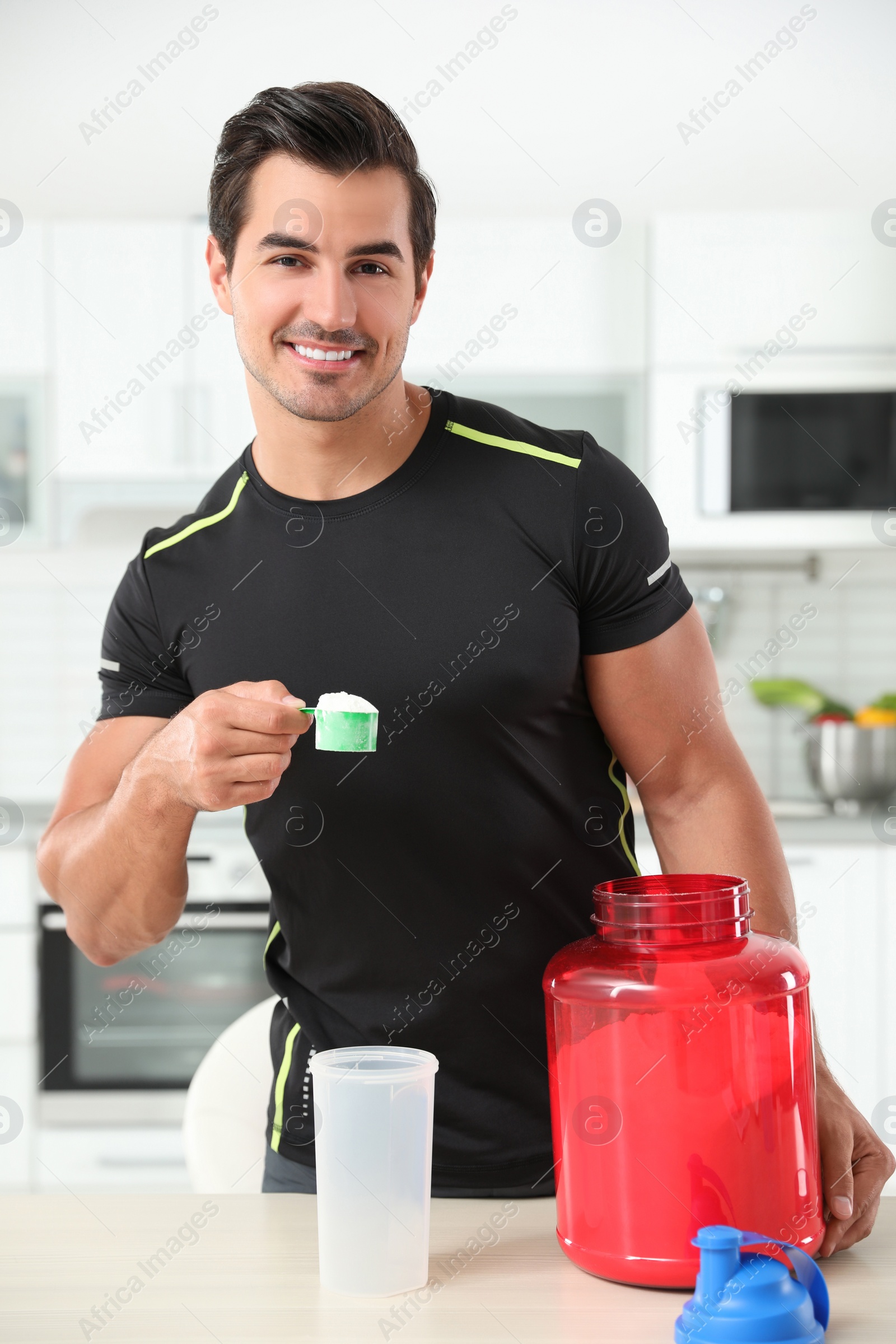 Photo of Young athletic man preparing protein shake in kitchen