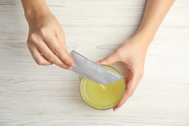 Photo of Woman pouring powder from medicine sachet into glass with water at table, top view