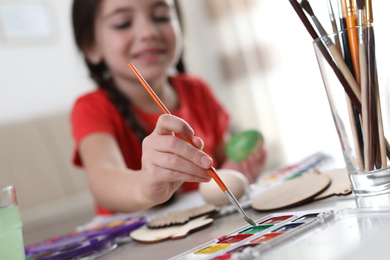 Photo of Little girl painting decorative egg at table indoors, focus on hand. Creative hobby