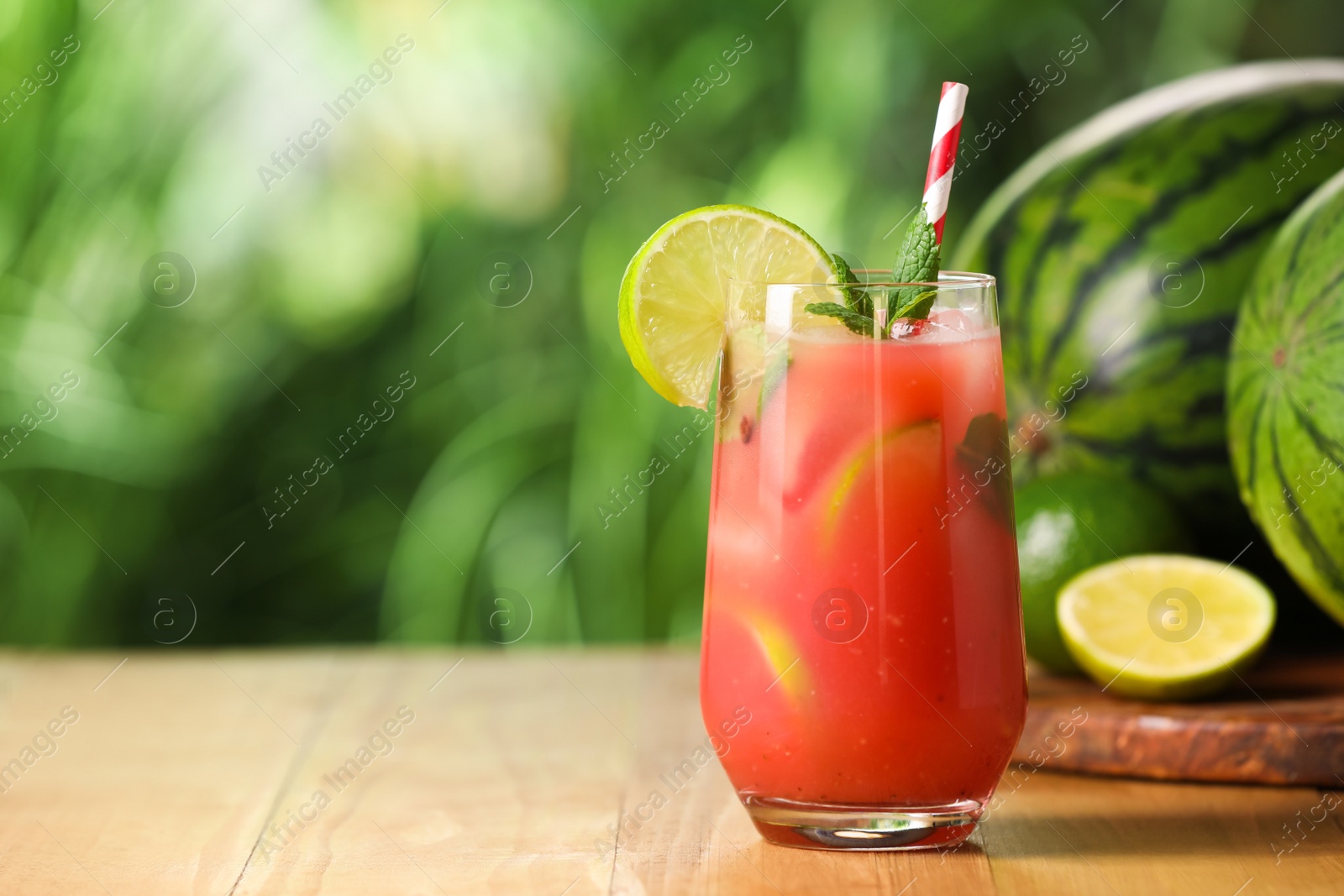 Photo of Glass of freshly made watermelon juice with lime and mint on wooden table outdoors, space for text