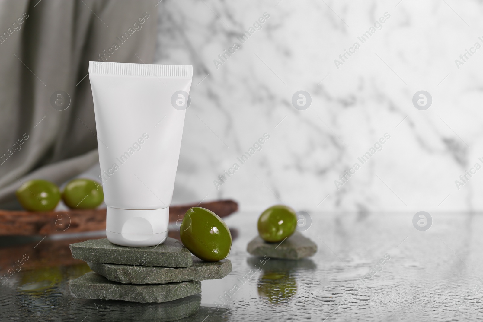 Photo of Tube of natural cream and olive on stones against white marble background, space for text