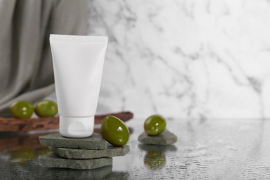 Photo of Tube of natural cream and olive on stones against white marble background, space for text