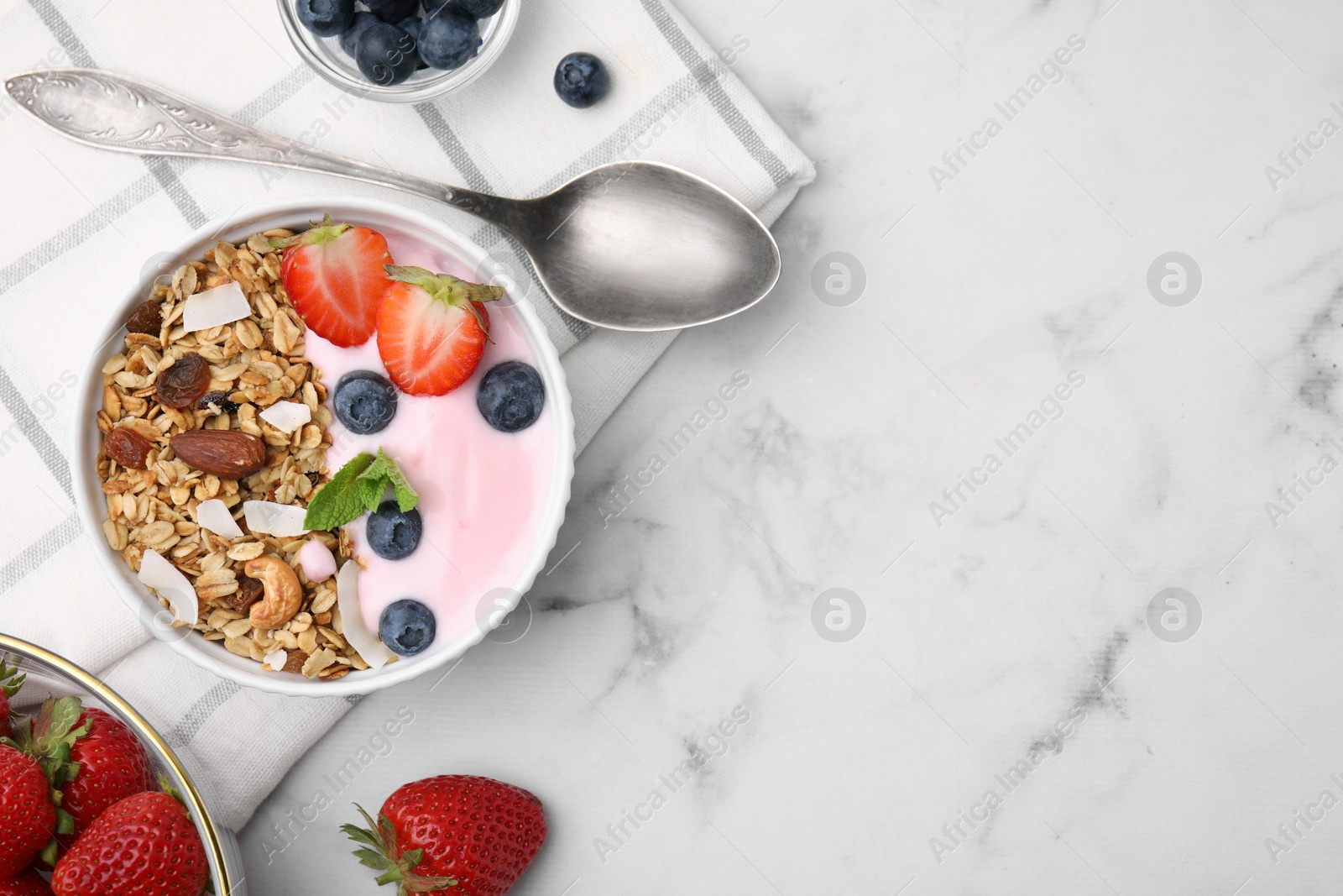 Photo of Tasty granola, yogurt and fresh berries in bowl served on white marble table, flat lay with space for text. Healthy breakfast