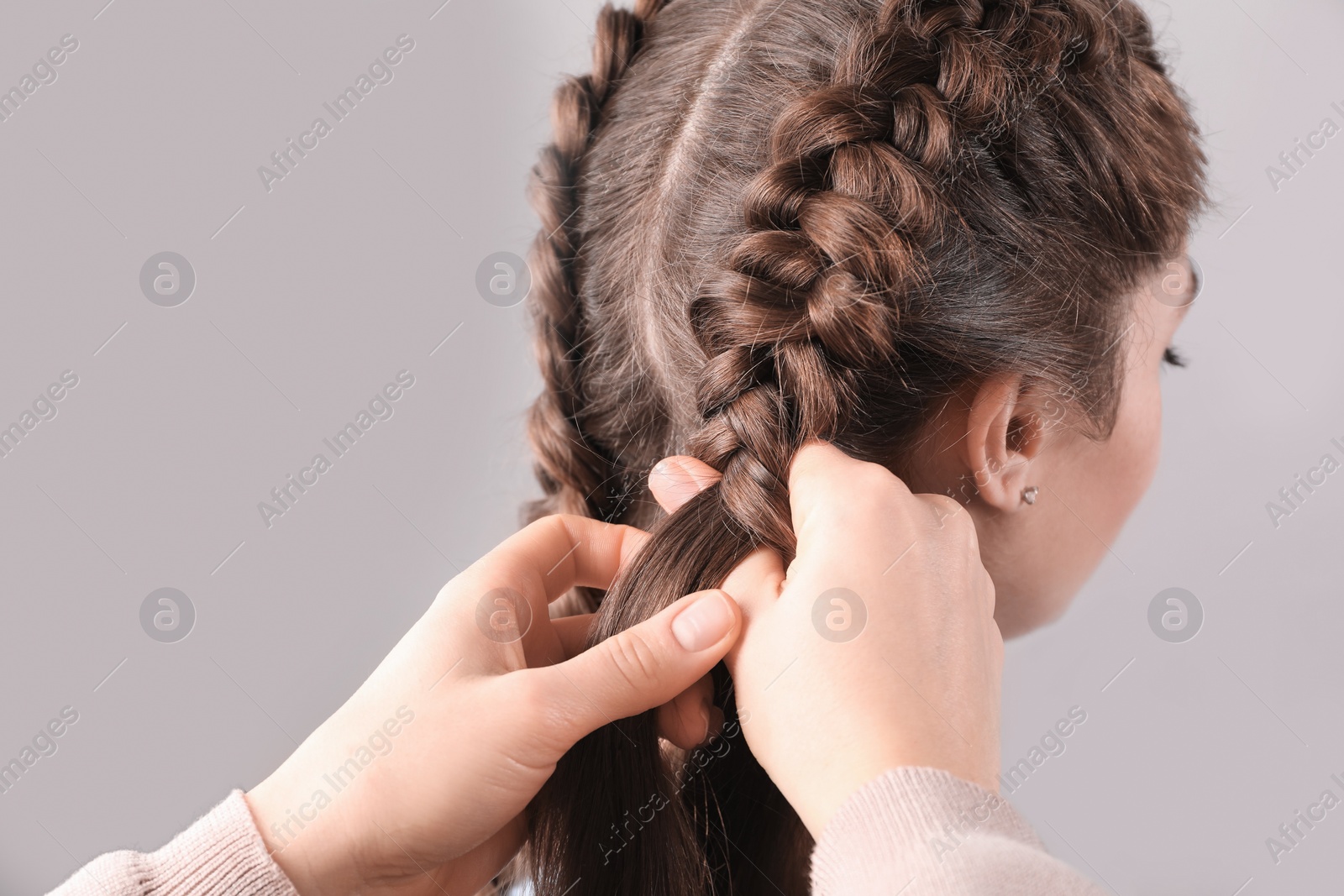 Photo of Professional stylist braiding woman's hair on grey background, closeup