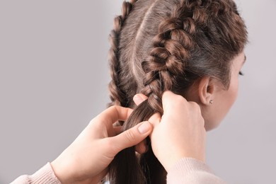 Professional stylist braiding woman's hair on grey background, closeup