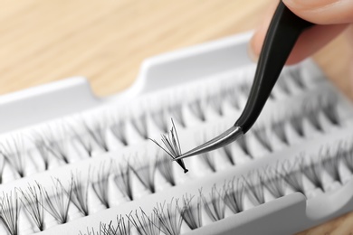 Woman holding tweezers with false eyelash, closeup