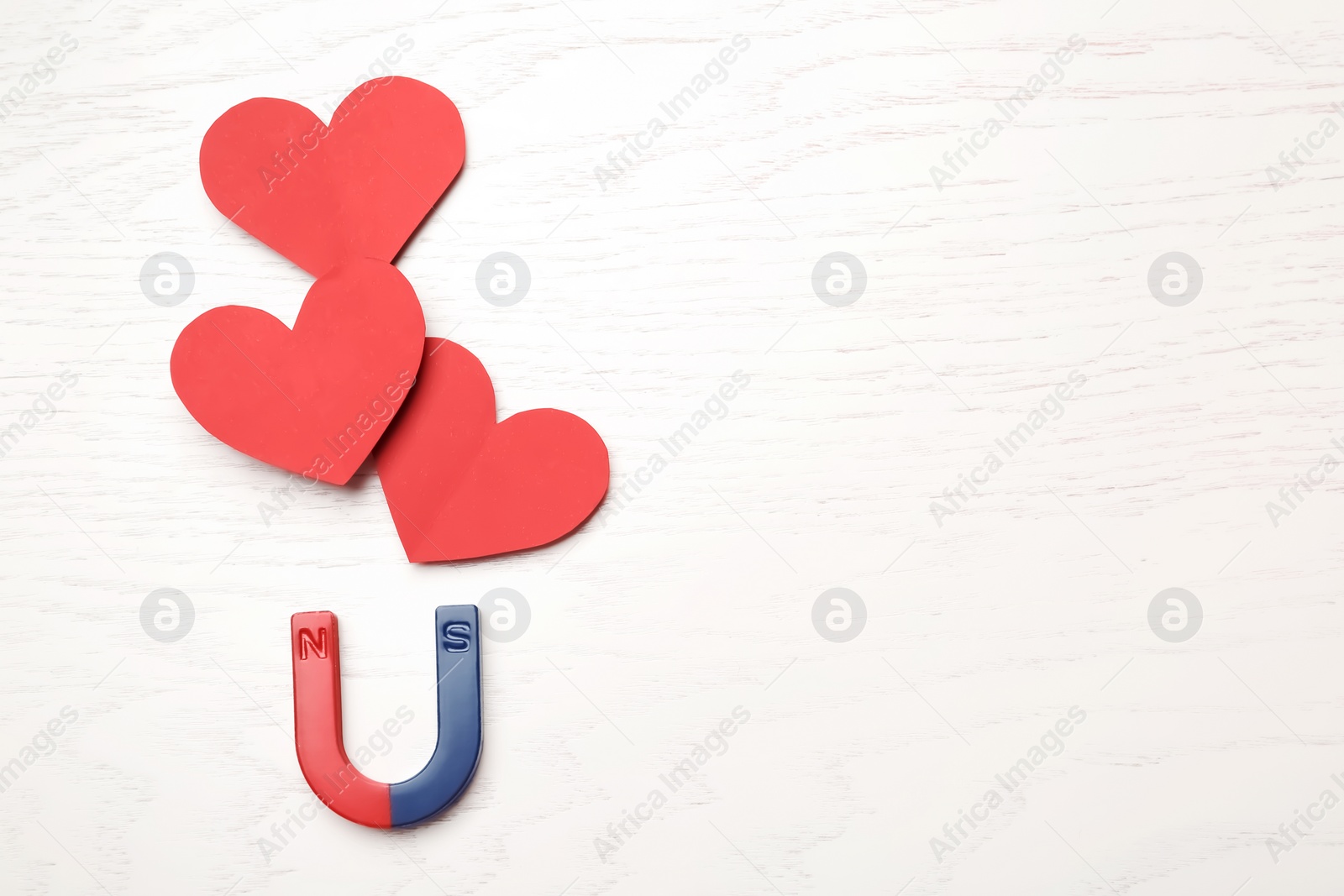 Photo of Magnet attracting red hearts on wooden background, top view with space for text. Love concept