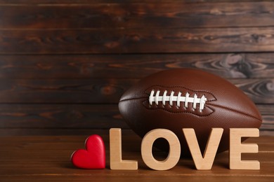 Photo of American football ball, heart and word Love on wooden table. Space for text