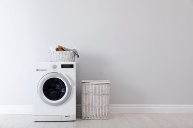 Photo of Washing machine with laundry and basket near wall. Space for text