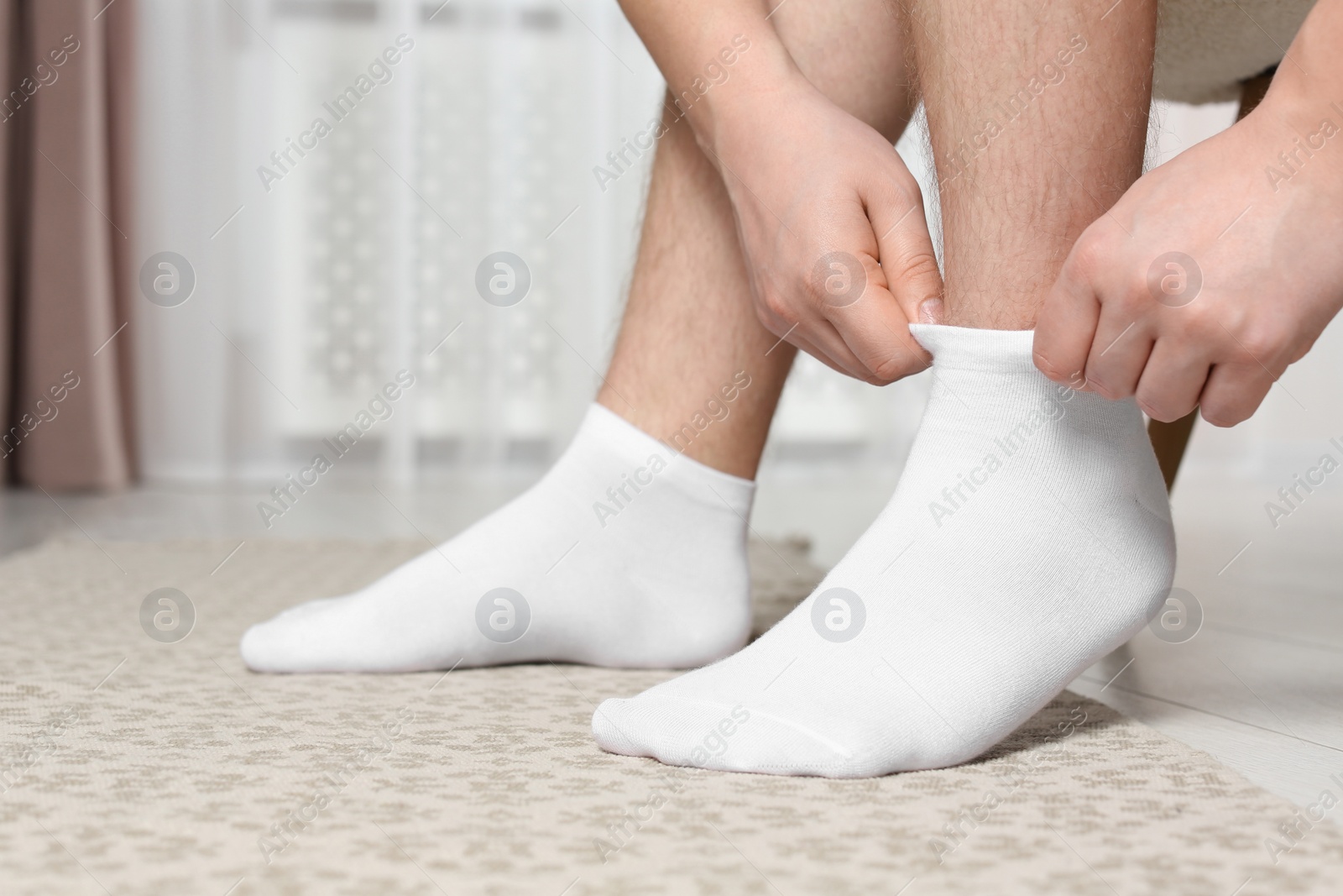 Photo of Man putting on white socks at home, closeup