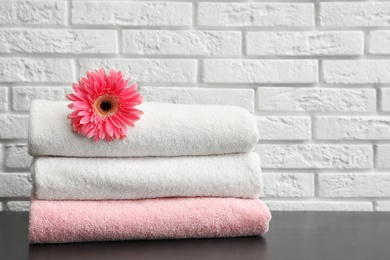 Stack of folded soft towels with flower on table near brick wall. Space for text