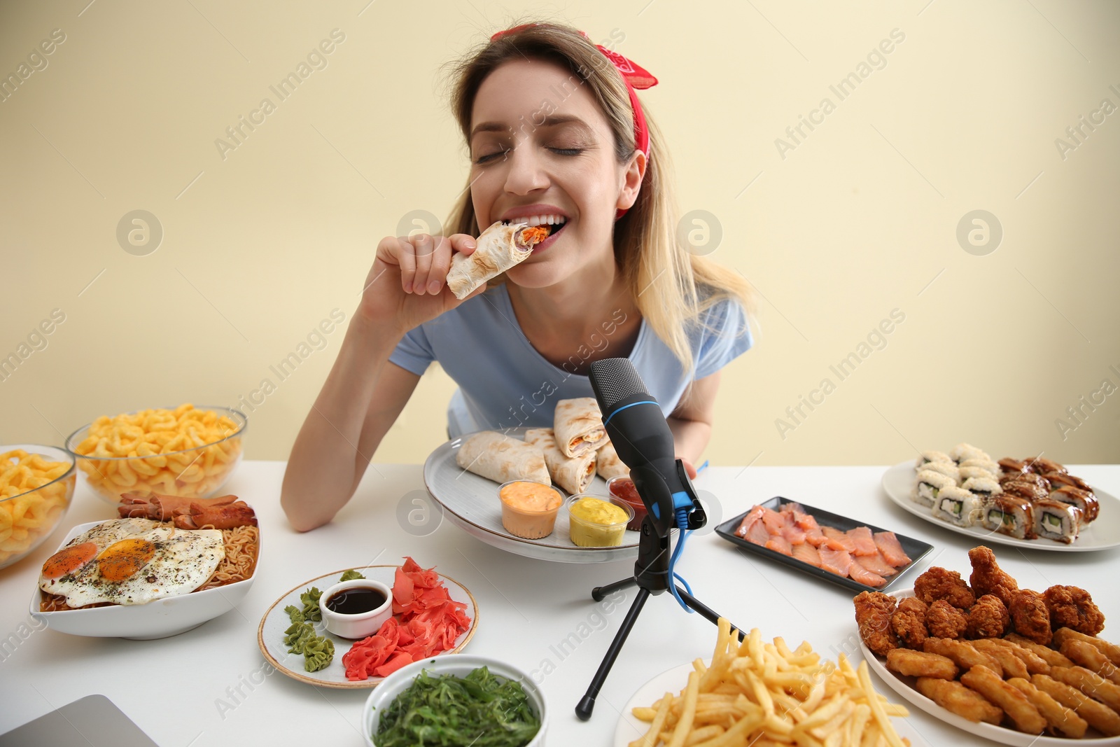 Photo of Food blogger eating in front of microphone at table against light background. Mukbang vlog