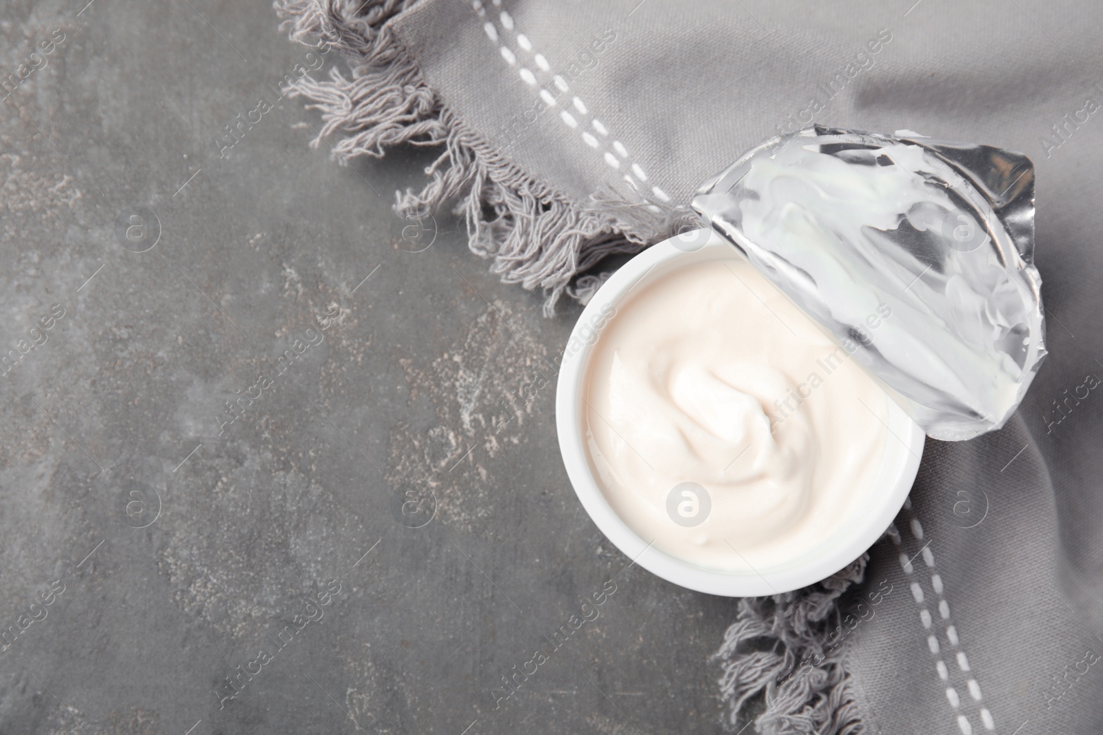 Photo of Plastic cup of fresh yogurt and napkin on grey background, top view. Space for text