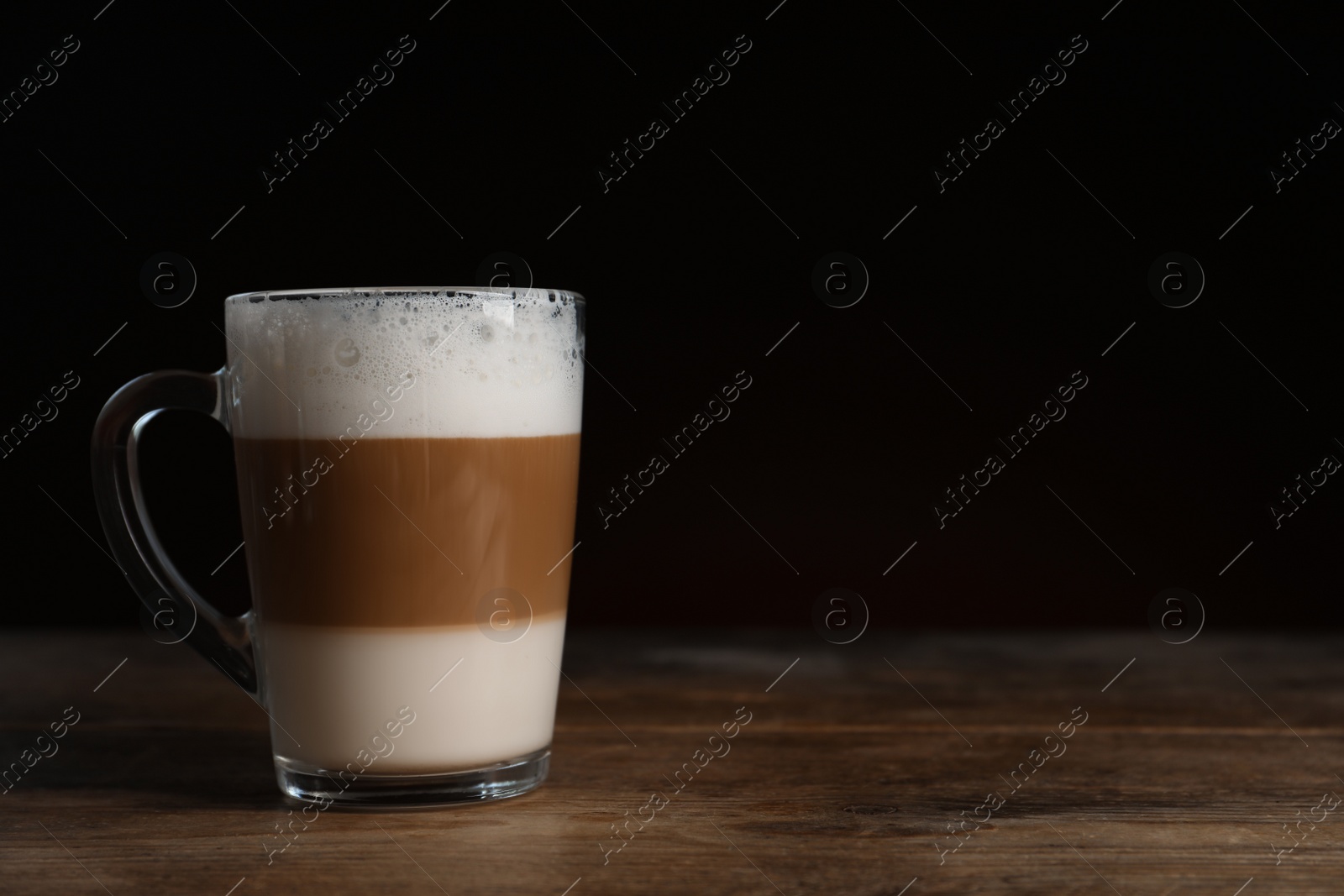 Photo of Glass cup of delicious layered coffee on wooden table against dark background, space for text