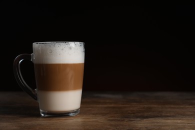 Glass cup of delicious layered coffee on wooden table against dark background, space for text