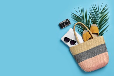 Photo of Wicker bag, camera, palm leaves and beach accessories on light blue background, flat lay. Space for text