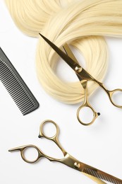 Professional hairdresser scissors and comb with blonde hair strand on white background, flat lay