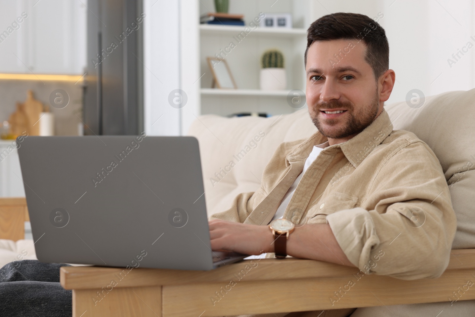 Photo of Happy man working with laptop on sofa in room