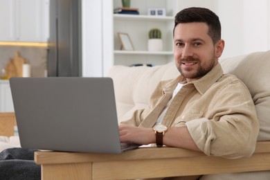 Happy man working with laptop on sofa in room