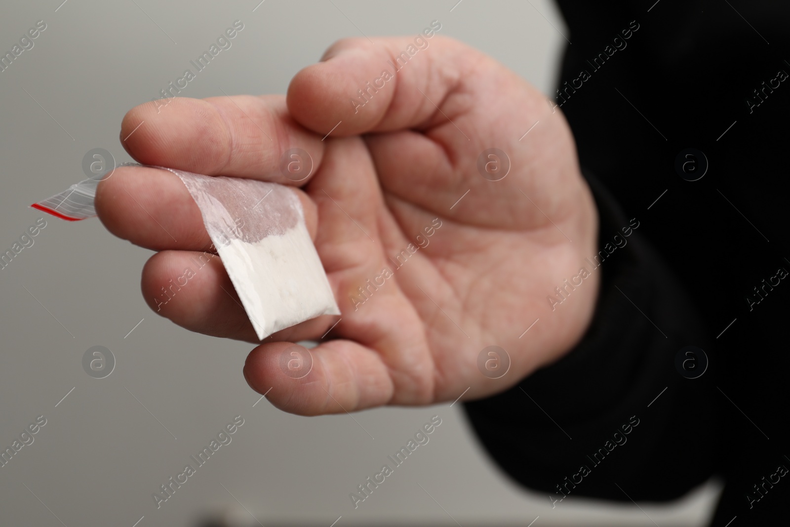 Photo of Drug addiction. Man with plastic bag of cocaine on light grey background, closeup